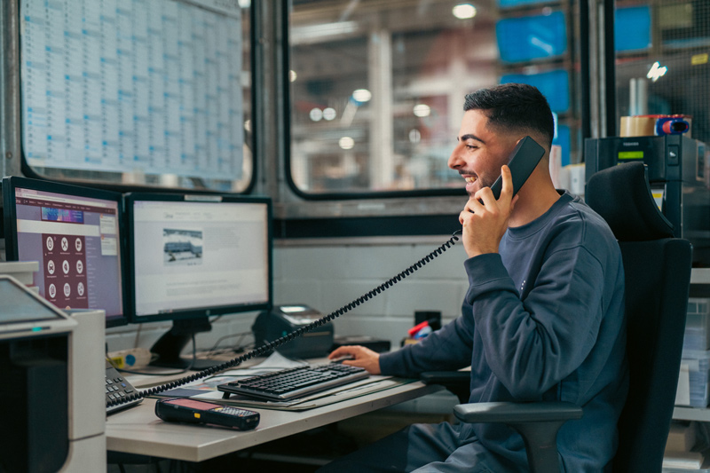 Ein Auszubildender arbeitet am Computer und telefoniert im Büro des Unternehmens